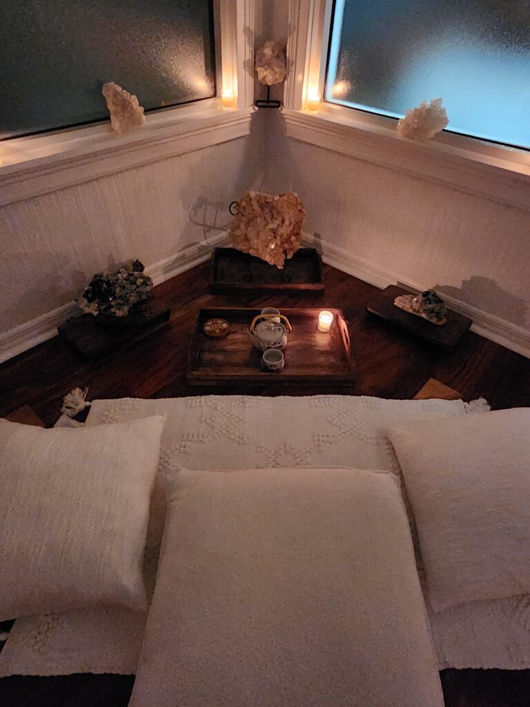 A corner of a room with a white couch and wooden floor.